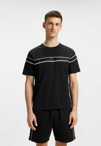 Black T-shirt with crew neck features horizontal stripes in gold and white, and a "BOSS" logo in the center. Paired with black shorts.