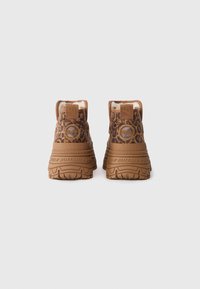 Par de botas de plataforma de color marrón con estampado de leopardo, con suelas gruesas y la marca "Buffalo" sobre un fondo blanco, visto desde la parte trasera.