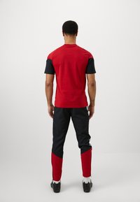 Sarkans un melns sporta tops ar īsām piedurknēm, apvienots ar melnām biksēm ar sarkaniem akcentiem pie kājām. Materiāls šķiet gluds un pieguļošs.