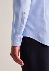 Camicia azzurra a maniche lunghe con polsini abbottonati, realizzata in cotone, caratterizzata da un design a polsino esagonale e un piccolo ricamo floreale nero.