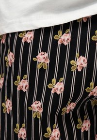 Tissu noir à rayures blanches verticales et petites roses roses avec des feuilles vertes, partiellement recouvert d'un tissu blanc.