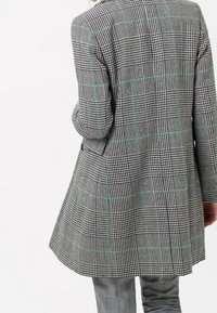 Blazer a scacchi grigi e neri con accenti verdi, caratterizzato da una vestibilità su misura, rever a punta e una silhouette svasata sul retro.