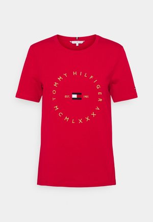 T-shirt rouge à manches courtes col rond avec texte jaune circulaire, "Tommy Hilfiger" et chiffres romains autour d'un petit logo rectangulaire rouge, blanc et bleu.