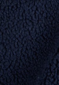 Dunkelblaues Fleece-Material mit einer strukturierten, weichen Oberfläche, die ein erhabenes Muster aufweist. Der Stoff wirkt plüschig und flauschig.