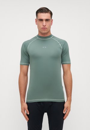 Ραφί, κοντό μανίκι, εφαρμοστό, σε ελιόχρωμο, κατασκευασμένο από απαλό, ελαστικό ύφασμα. Διαθέτει αντίθετη ραφή και ένα μικρό λογότυπο στο στήθος.