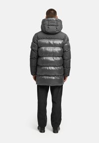 Padded grey winter jacket with a hood, featuring a glossy finish, horizontal stitching, and a longer length, worn over dark pants.