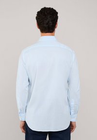 Camisa de manga larga azul claro con cuello abotonado, que presenta un tejido suave y ligeramente texturizado, y un dobladillo curvado en la parte posterior.