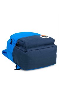 Mochila azul y marino con un compartimento superior y una sección inferior más grande. Presenta un parche con logo y dos cierres con cremallera. Tela duradera.