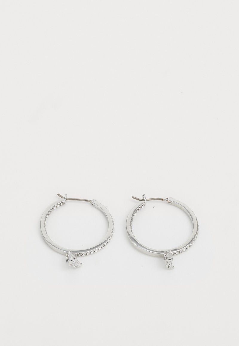 Brincos de argola em prata com um design torcido, acabamento em metal suave e um pequeno detalhe de charme com gemas claras incrustadas de um lado.