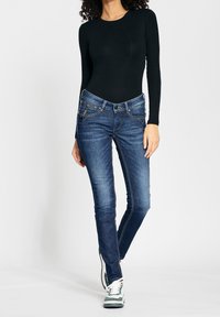 Dark blue denim jeans with a slim fit, featuring front pockets, detailed stitching, and a mid-rise waistband, paired with a black long-sleeve top.