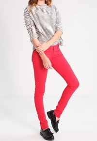 Vaqueros ajustados rojos con una textura suave combinados con una blusa de manga larga a rayas en blanco y negro. Mocasines negros completan el atuendo.