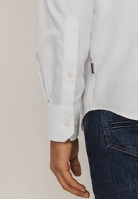 Witte blouse met lange mouwen en knoopmanchetten, van textuurstof met een gebogen zoom, gecombineerd met donkerblauwe spijkerbroek.