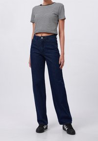 Camiseta corta de rayas en blanco y negro, combinada con jeans de mezclilla azul oscuro de talle alto y corte holgado. Zapatillas negras completan el conjunto.