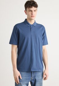 Μπλέ πόλο μπλούζα από βαμβάκι, με τρεις κουμπάκια, κοντά μανίκια και μικρό λογότυπο κεντημένο στο στήθος.