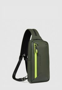Mochila verde con textura suave, que presenta una cremallera de neón contrastante y un diseño rectangular elegante. Incluye una correa negra ajustable.