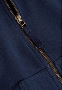 Námořnická modrá mikina na zip se zlatým kovovým zipem, s měkkou texturou a klokanní kapsou. Hladký povrch látky.
