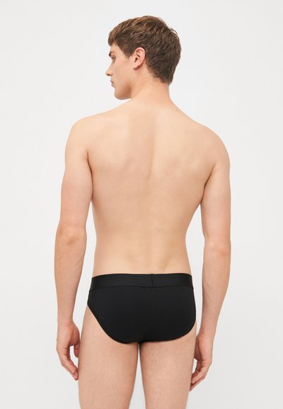 Black swim briefs with a smooth texture, featuring a wide waistband and a fitted design, displayed on a model from a rear perspective.