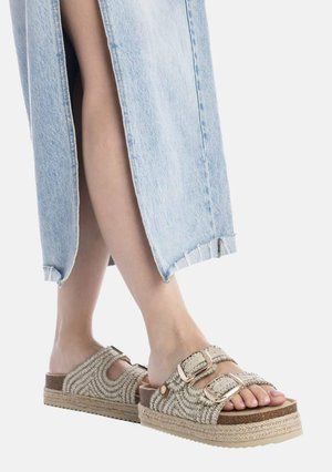 Persona che indossa pantaloni di jeans azzurri chiaro con spacco laterale e sandali platform beige intrecciati con due cinturini con fibbia.
