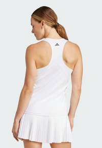 Rochie sport albă cu un top ajustat, design racerback și fustă plisată. Prezintă logo-ul Adidas pe spate. Textură de țesătură netedă.