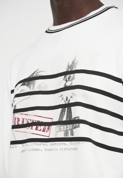 Λευκή μπλούζα φούτερ με μαύρες οριζόντιες ρίγες, με γραφικό σχέδιο ενός κινούμενου γάτου και τη σφραγίδα «BUSTED». Το κείμενο περιλαμβάνει λεπτομέρειες για τον χαρακτήρα.