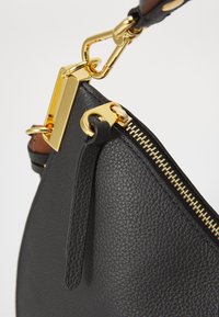 Black textured leather handbag with gold-tone hardware, featuring a zipped closure and detailed stitching. Adjustable strap included.