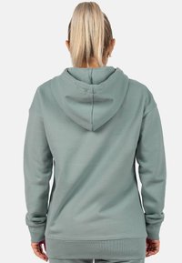 Felpa con cappuccio verde chiaro, dal fit rilassato, con maniche lunghe e polsi a costine. Il tessuto appare morbido con una sottile texture.