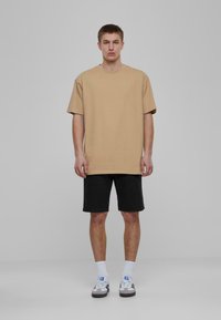 Bēša oversize T-kreklu, īsas piedurknes, kopā ar melniem šortiem, baltām zeķēm un melnbaltiem čības. Vienkāršs dizains, brīva piegriezuma.