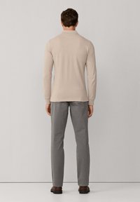 Polo beige à manches longues associé à un pantalon gris. Le polo possède un col classique, et le pantalon présente une coupe slim.