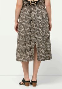 Jupe noir et beige arrivee au genou avec un motif texturé et une fente à l'arrière. Associée à des chaussures noires à talons carrés.