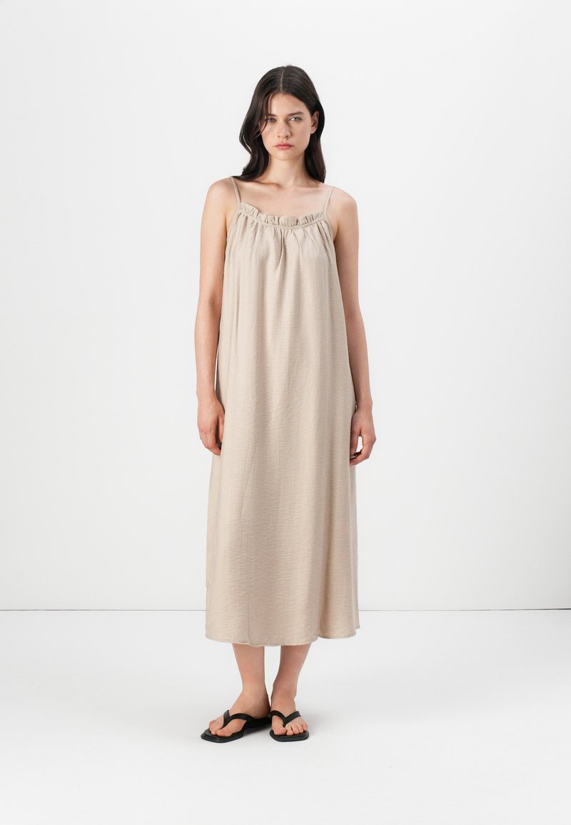 Duga, bež haljina od lagane tkanine s nabranu dekolteom i tankim naramenicama, s opuštenim krojem i maksi dužinom.