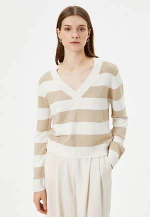 Beige og hvidstribet strikket sweater med V-udskæring, lange ærmer og ribbet kant. Bæres med cremfargede bukser.