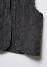 Prošívaná vesta v tmavě šedé barvě s diamantovým vzorem, vyrobená z texturované tkaniny. Má zaoblené okraje a žádné viditelné zapínání.