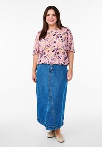 Blusa floreale rosa con motivi viola e verdi, abbinata a una lunga gonna in denim blu. Scarpe flat beige completano l'outfit.