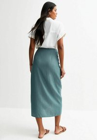 Teal midi skirt with textured fabric, elastic waistband, paired with a loose-fitting white shirt and brown sandals. Back view displayed.