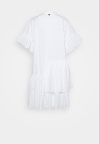 Robe blanche à manches courtes avec manches volantées et ourlet asymétrique à volants superposés, vue de dos sur un fond uni.