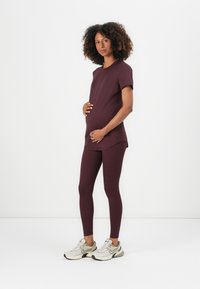Mammaklærsett i mørk burgunder; t-skjorte med kort erme og buet hem, kombinert med tettsittende leggings og lyse joggesko.