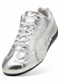 Chaussure de sport argentée avec une finition métallique brillante, lacets blancs et semelle noire. Présente le logo Puma sur le côté et la languette.