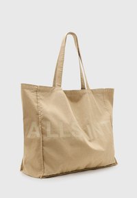 Beige Canvas-Shopper-Tasche mit großem, hell gefärbtem "ALLSAINT"-Text an der Seite und zwei stabilen Tragetaschen.