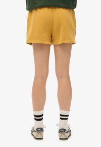 Shorts en coton jaune avec une finition légèrement texturée. Dotés d'une taille élastique et d'un ourlet simple. Associés à des chaussettes blanches et des accents rayés.