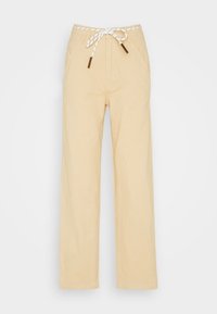 Béžové bavlněné kalhoty širokého střihu s bílým provázkem na stahování a hnědými kovovými konci, které mají dvě přední kapsy a hladkou texturu.