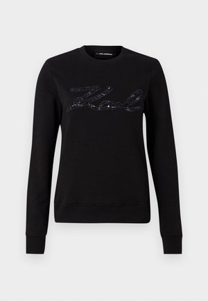Sweatshirt noir à manches longues, avec un design de logo texturé en sequins noirs sur la poitrine. Encolure ronde et poignets côtelés.