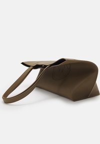 Sac à main en cuir marron avec une bandoulière simple et une fermeture à rabat, reposant sur le côté sur un fond blanc.