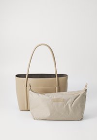 Borsa tote beige con esterno liscio e manici lunghi, accompagnata da una borsa a tracolla più piccola, morbida e con zip, entrambe con un logo discreto.