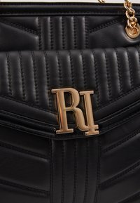 Sac à main en cuir noir avec texture matelassée, logo en métal doré et détails cousus, doté d'un rabat structuré.