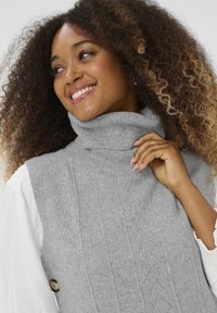 Sivi turtleneck pulover s rebrastom teksturom i dijamantnim uzorkom. Mekani, udobni materijal s ležernim krojem i detaljem dugmeta sa strane.