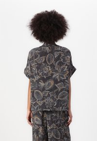 Lässig geschnittene Bluse mit Blumenmuster aus dunklem Stoff, verziert mit filigranen goldenen und weißen Mustern, kurzärmlig und mit einer weichen, strukturierten Oberfläche.
