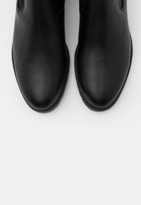 Botas de tobillo de piel negra con una superficie lisa, punta redonda y paneles laterales elásticos. Suela de goma duradera para mayor tracción.