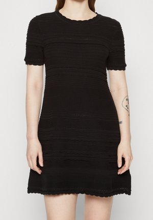 Abito in maglia nera con maniche corte, caratterizzato da una texture a coste e bordi ondulati. Il motivo include righe orizzontali e un colletto rotondo.