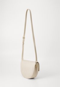 Beige crossover-veske med en buet form og teksturert, preget logodesign. Justerbar stropp og gullfargede detaljer.
