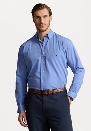 Lichtblauw overhemden met lange mouwen en een klein logo op de borst, gecombineerd met donkere broeken en een leren riem in bruin.